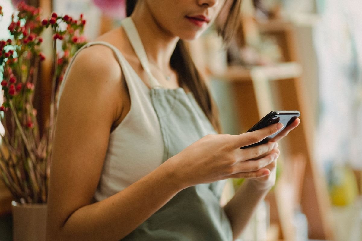 Une commerçante en tablier consulte son téléphone dans sa boutique